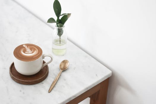 pexels-photo-3554240-3554240 A cappuccino on a marble table with a plant and spoon, exuding a minimalist vibe.